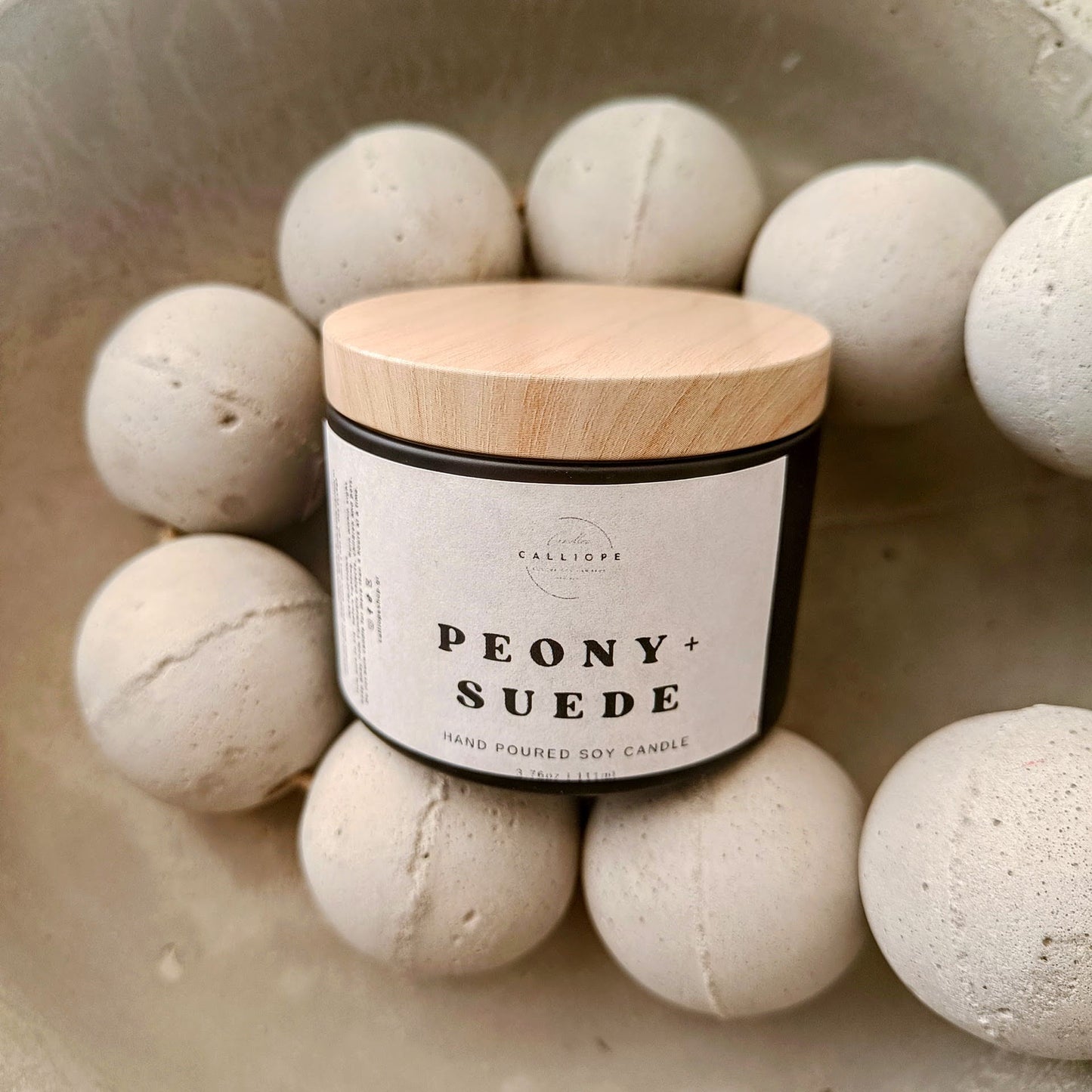 A set of four black tins with lids containing soy candles in different fragrances, labeled respectively as Orange Patchouli, Vanilla, Peony, and Amber.