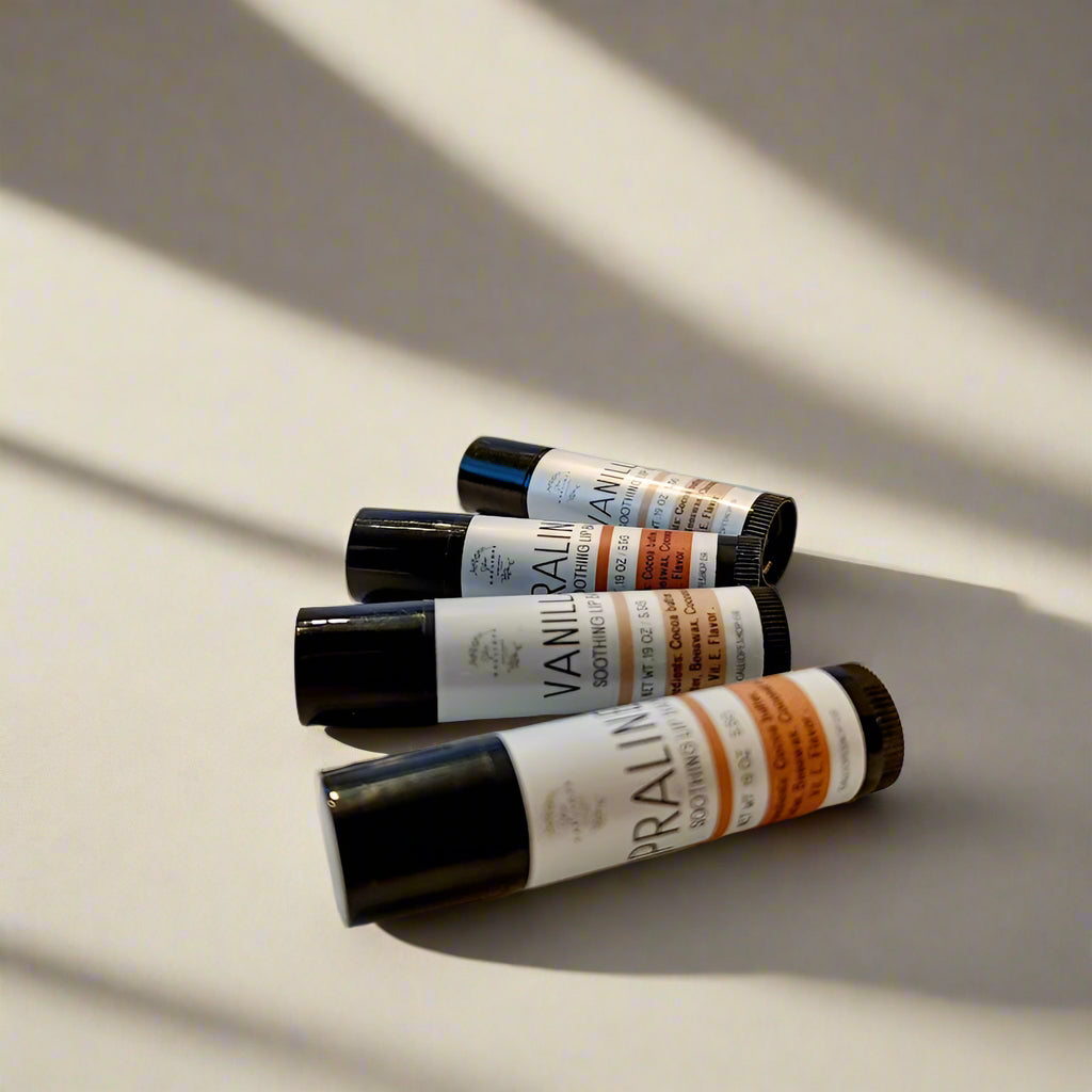 Three containers of 'Vanilla & Praline' lip balm with matte black and white labels, positioned on a light background.