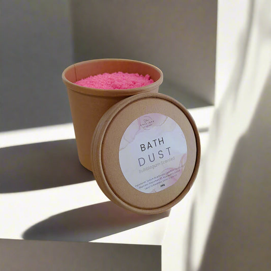 Bowl of pink bath dust with a brown paper cup on a white background