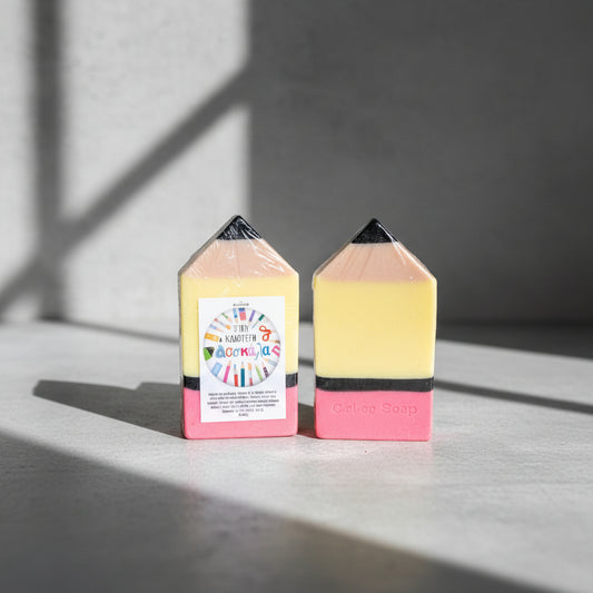 Two colorful soap bars shaped like pencils on a cement surface with a neutral background