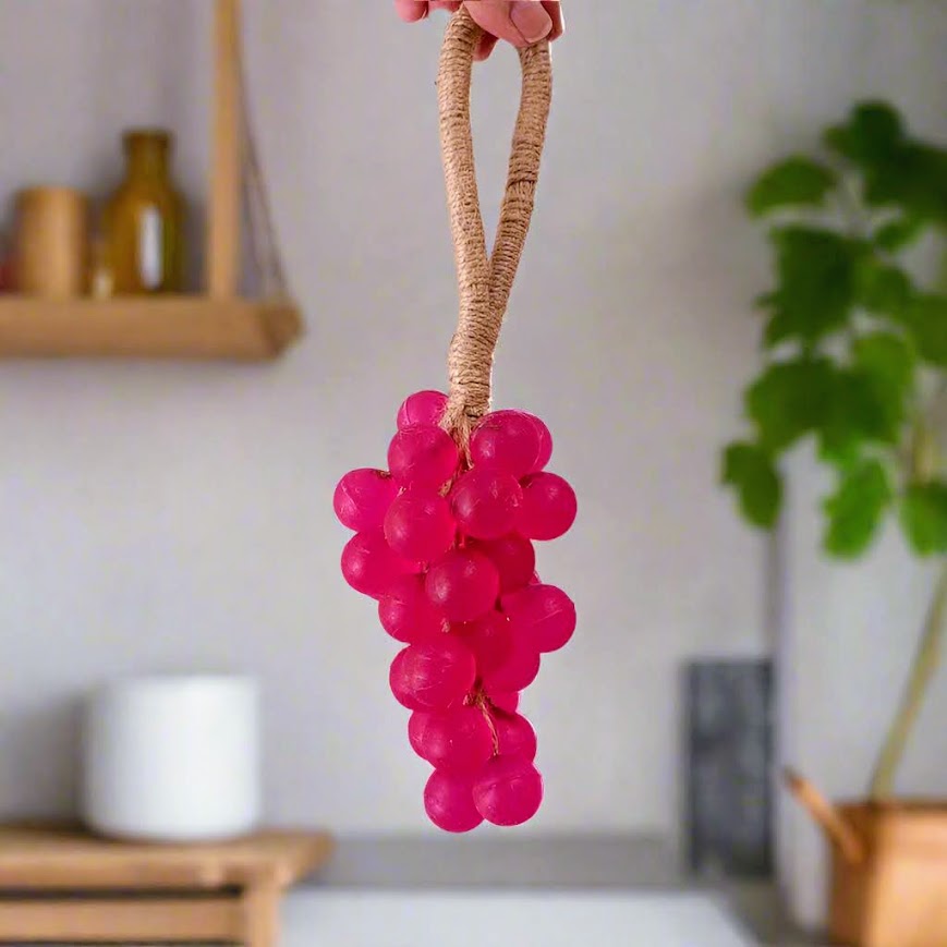 Pink toy shaped like grapes held by a hand in a kitchen setting