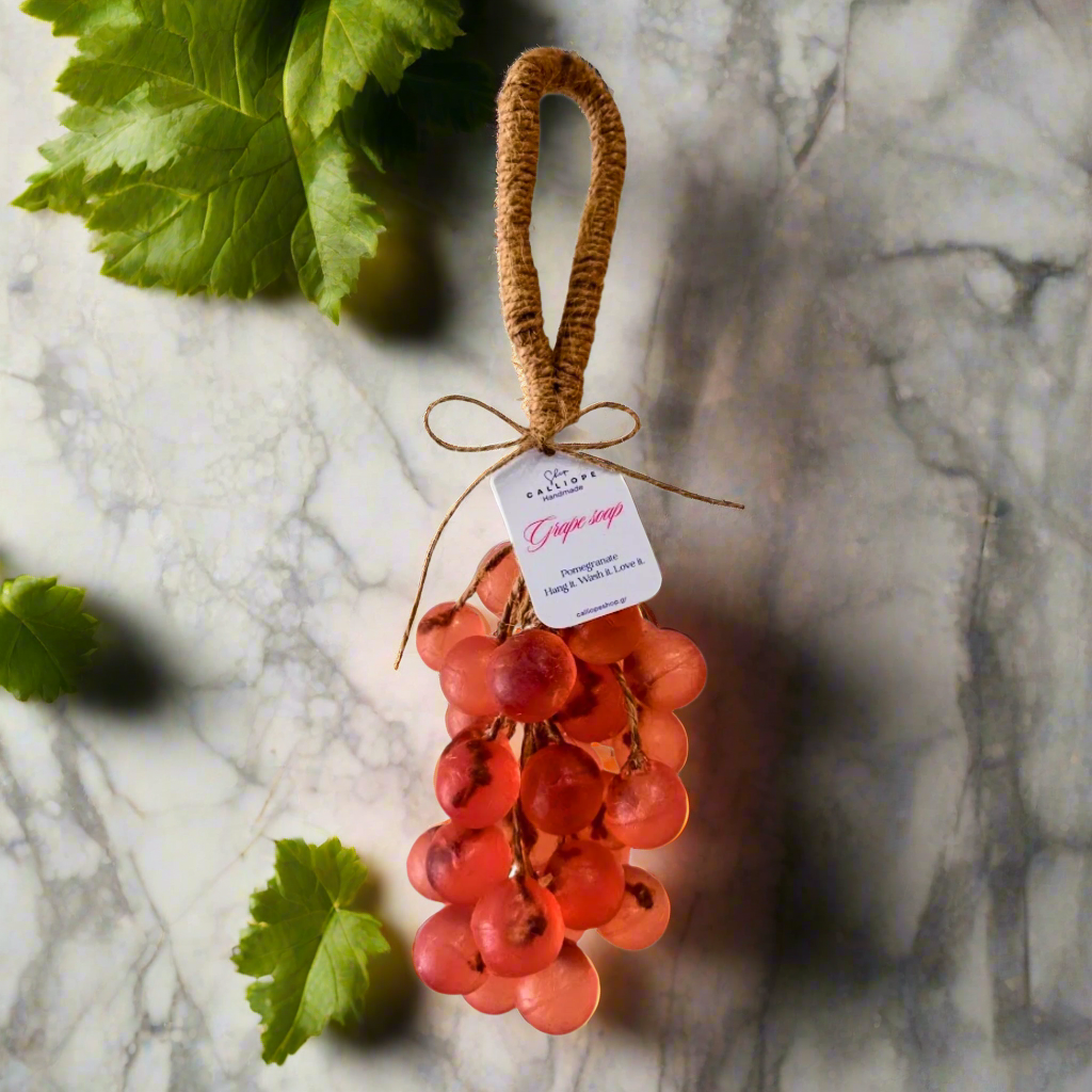Handmade soap shaped like a bunch of red grapes with a tag on a marble surface.