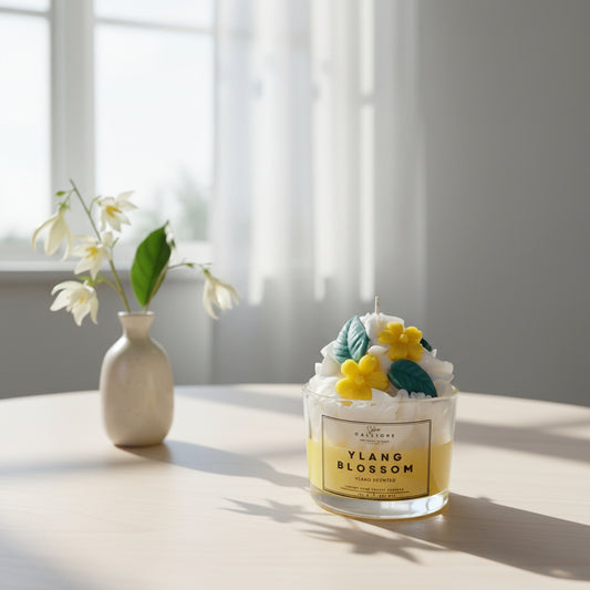 Candle labeled 'Ylang Blossom' with decorative elements on a table next to a vase with flowers.