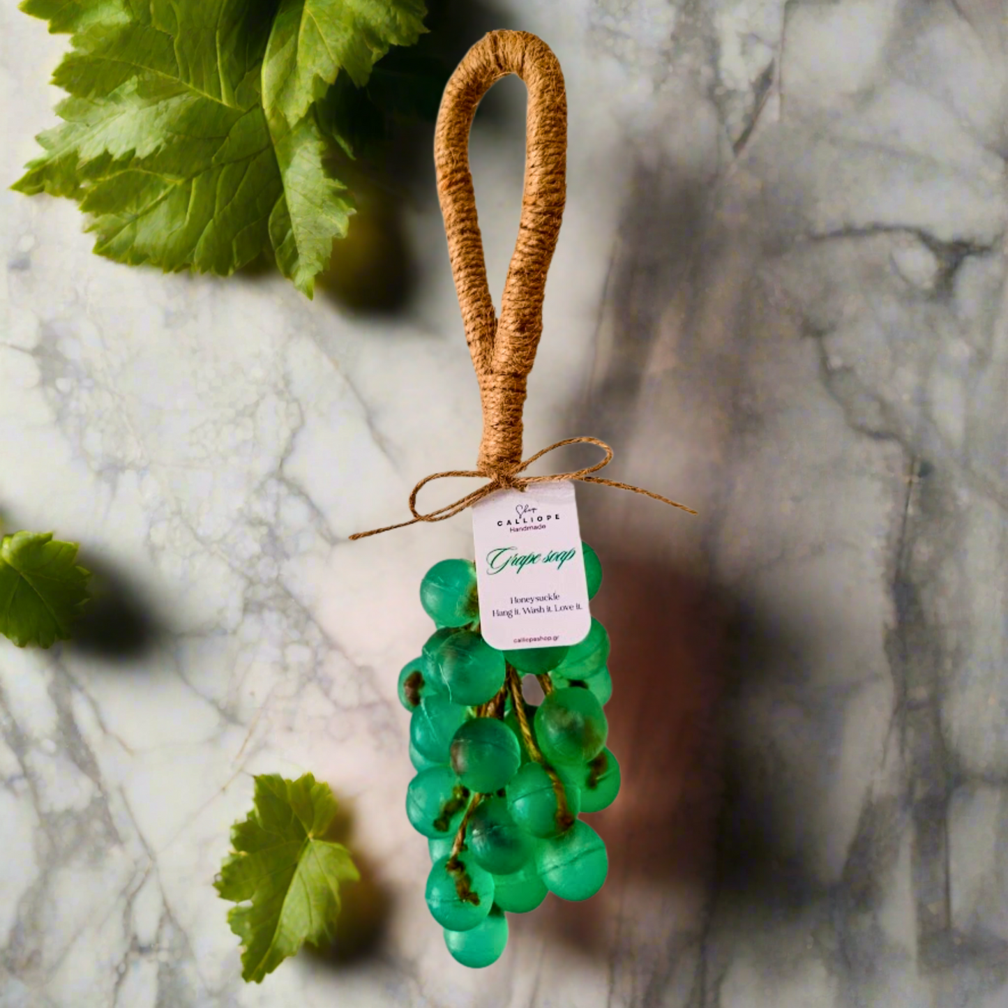 Decorative green grape-shaped soap with a brown handle on a marble surface.