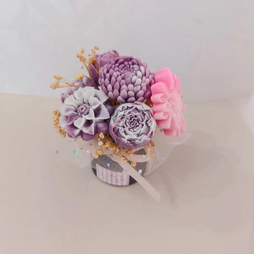 Decorative flower arrangement with purple, pink, and white flowers in a small pot on a light background