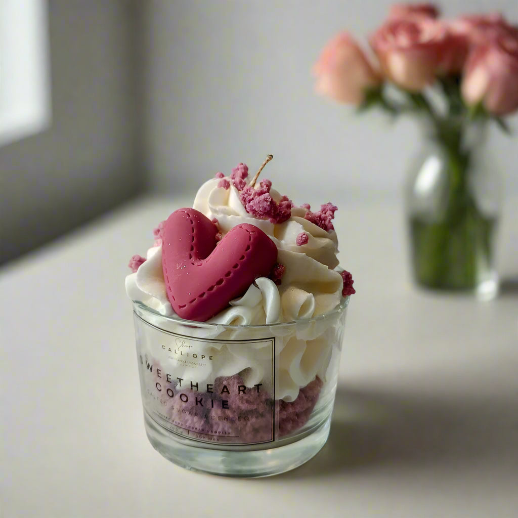 Handmade soy wax candle in a clear glass jar with decorative heart-shaped toppings, with a background of roses.