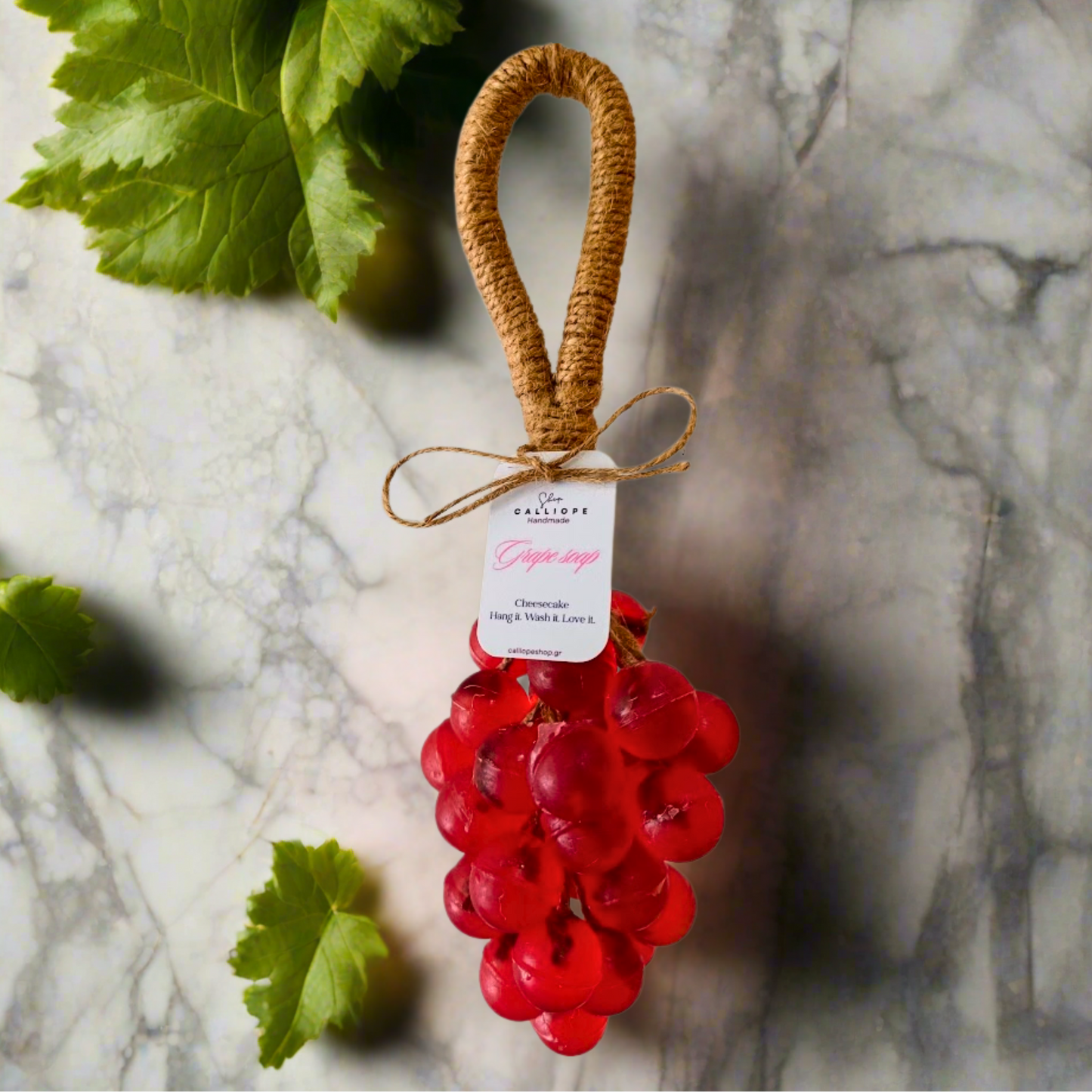 Decorative red grape soap with a brown handle on a marble surface