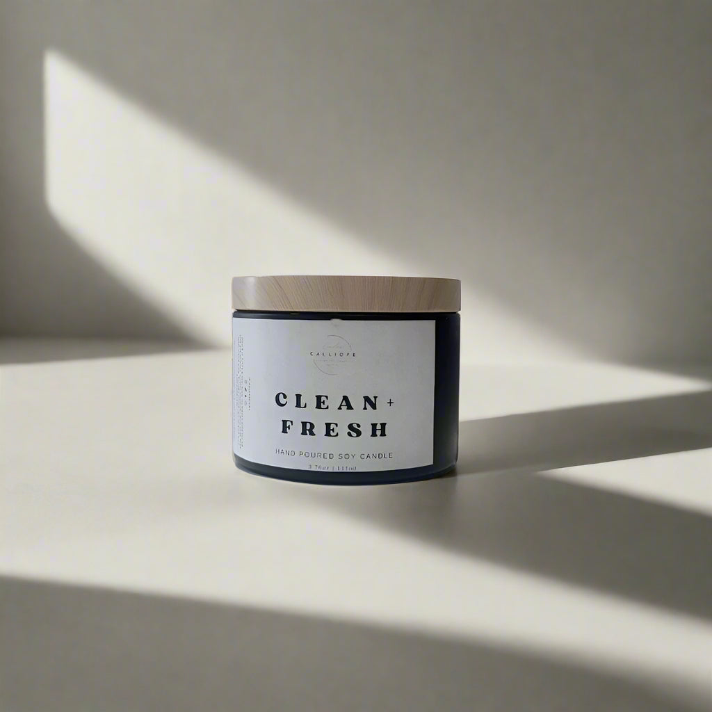 Candle jar labeled 'Clean + Fresh' on a white surface with a light gray background