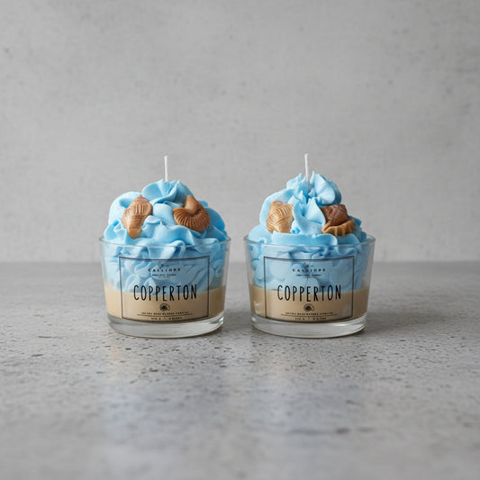 Two blue-themed candles with shell figures in glass containers on a concrete surface.