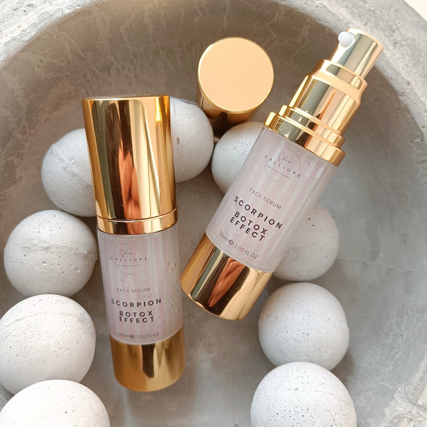 A gold-colored bottle with a pump dispenser labeled 'Scorpion Botox Effect Serum' in a cement bowl with cement beads.