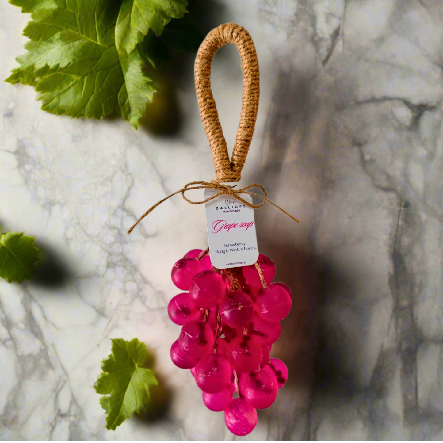 Handmade pink grape soap with a raffia handle on a marble surface.