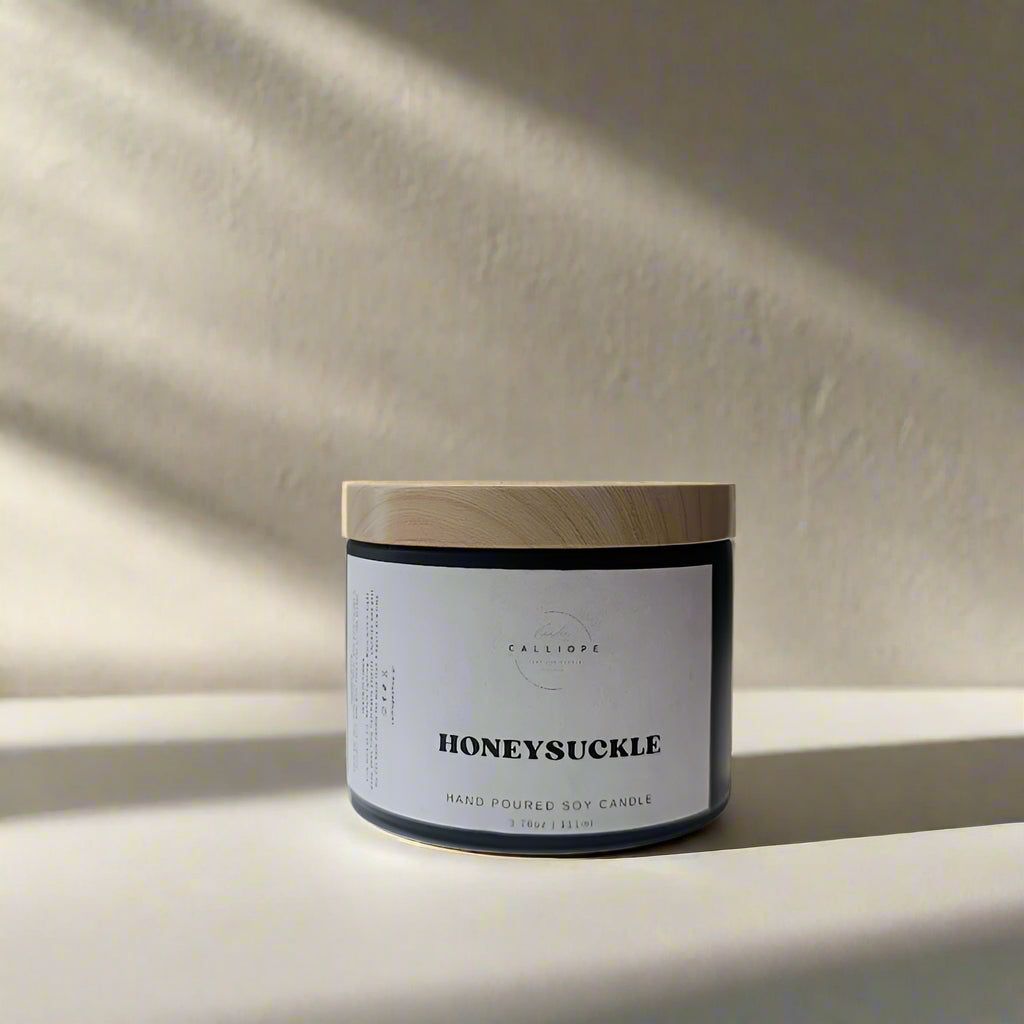 Candle jar labeled 'Honeysuckle' on a white surface with a neutral background