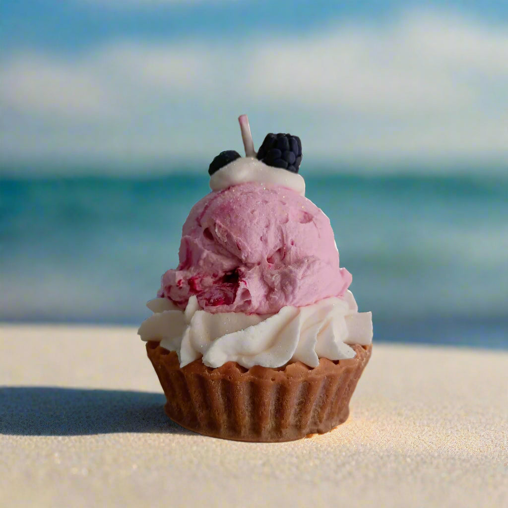 Ice cream cupcake with pink and white frosting on a sandy beach with ocean in the background