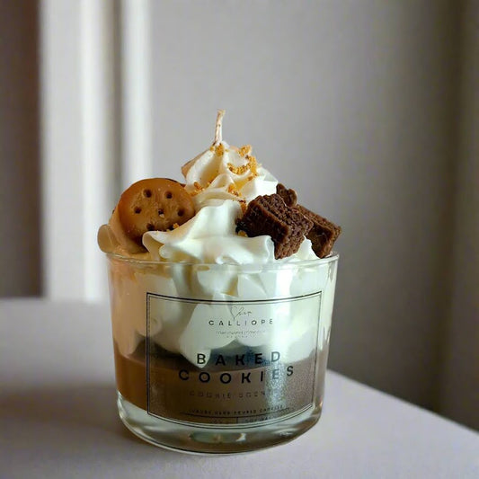 Glass jar filled with a dessert candle topped with whipped cream, cookies, and a candle, on a neutral background.