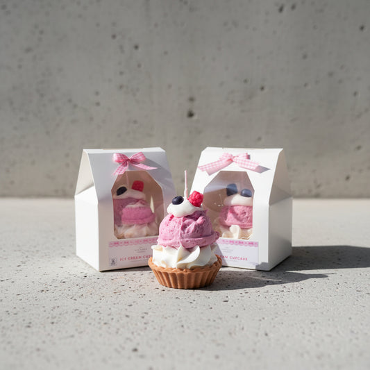 Cupcake candle with pink frosting and berries on top, displayed in front of its packaging.