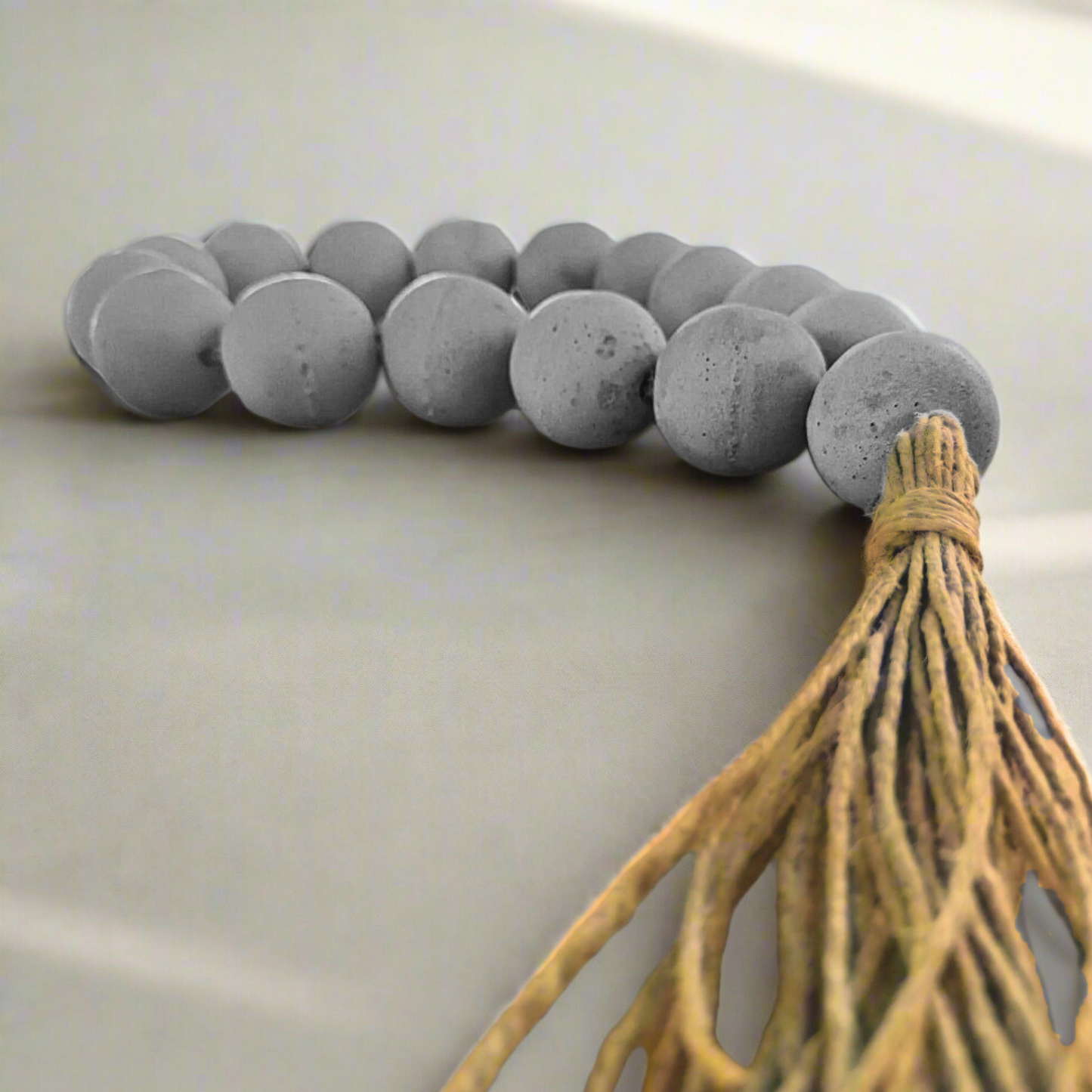 Decorative item with gray beads and a tassel on a light background