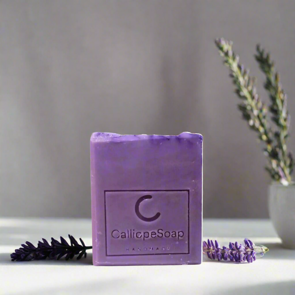 A bar of lavender-scented soap with 'CALLIOPE SOAP' branding, placed on a surface with some lavender flowers in the background.