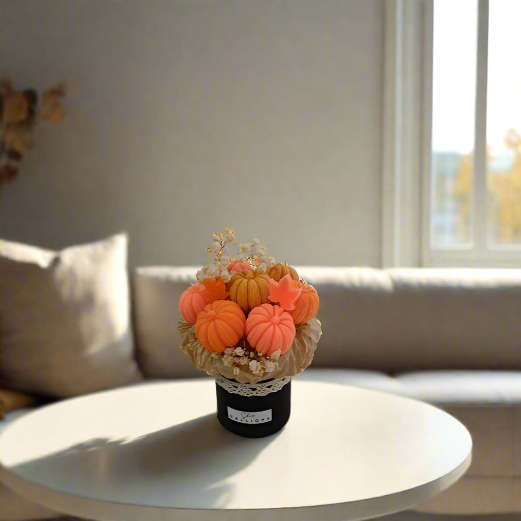Decorative arrangement of small pumpkins and flowers on a white surface with a blurred background.