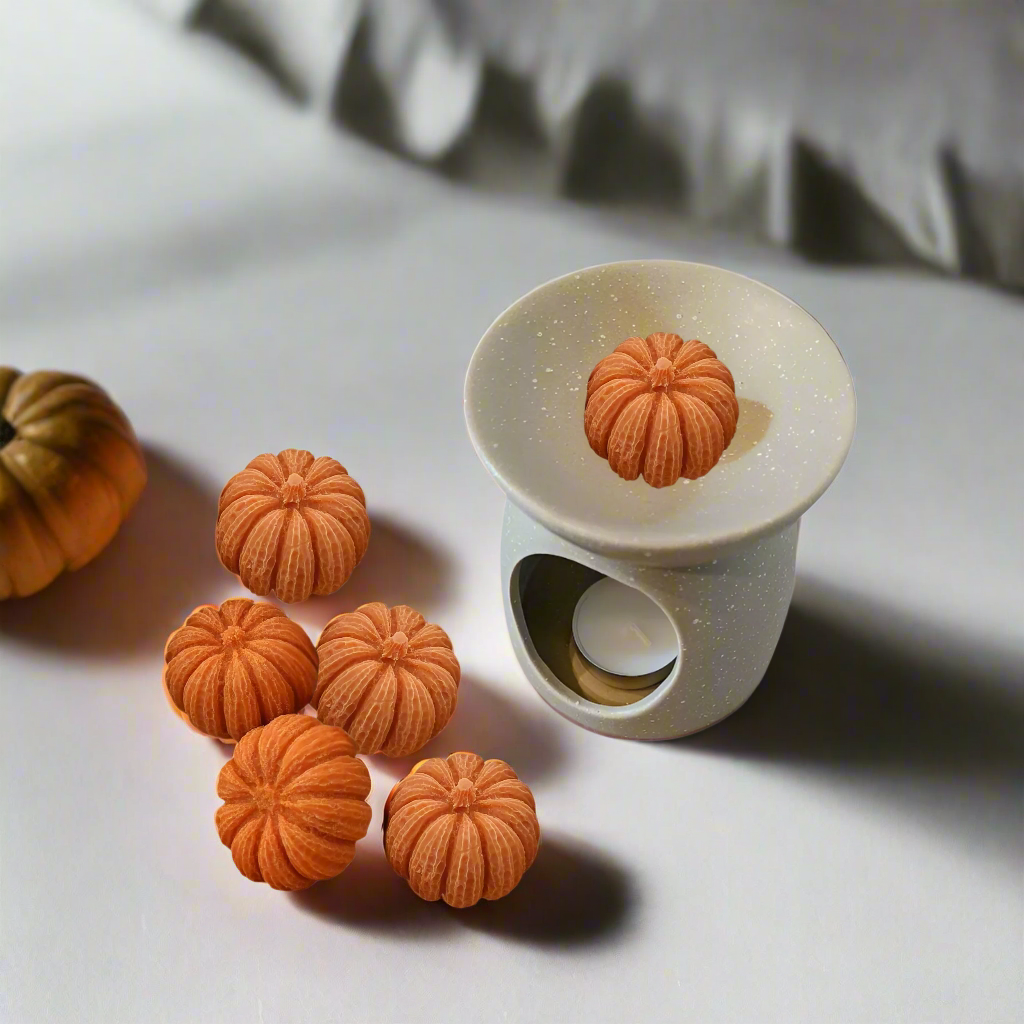 White ceramic mold with orange pumpkin-shaped cavities on a light surface.