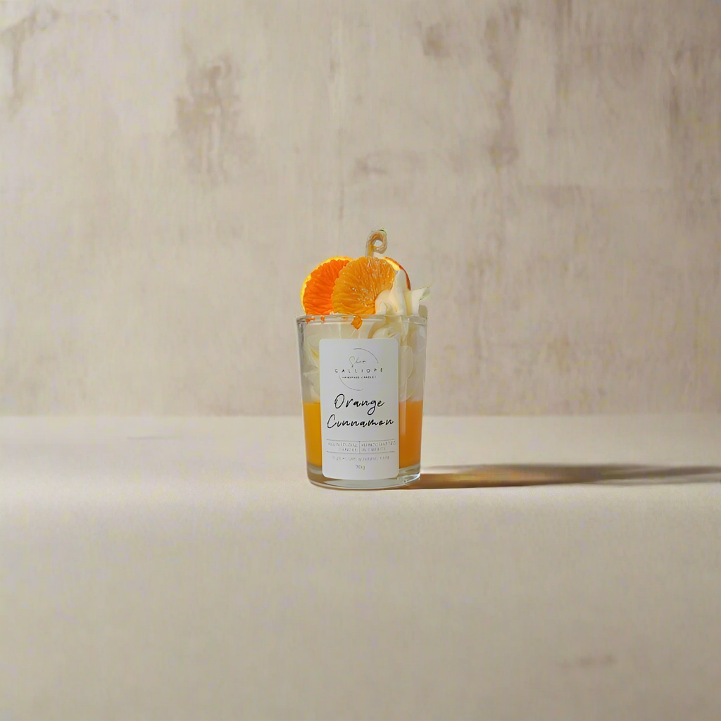 Glass shot candle with orange and cinnamon sticks on a neutral background