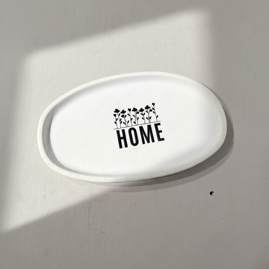 White oval ceramic plate with 'HOME' and floral design on a gray background