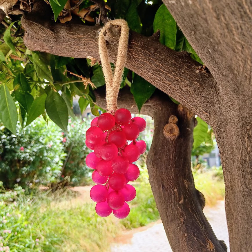Bunch of pink grapes hanging from a branch with green leaves in the background