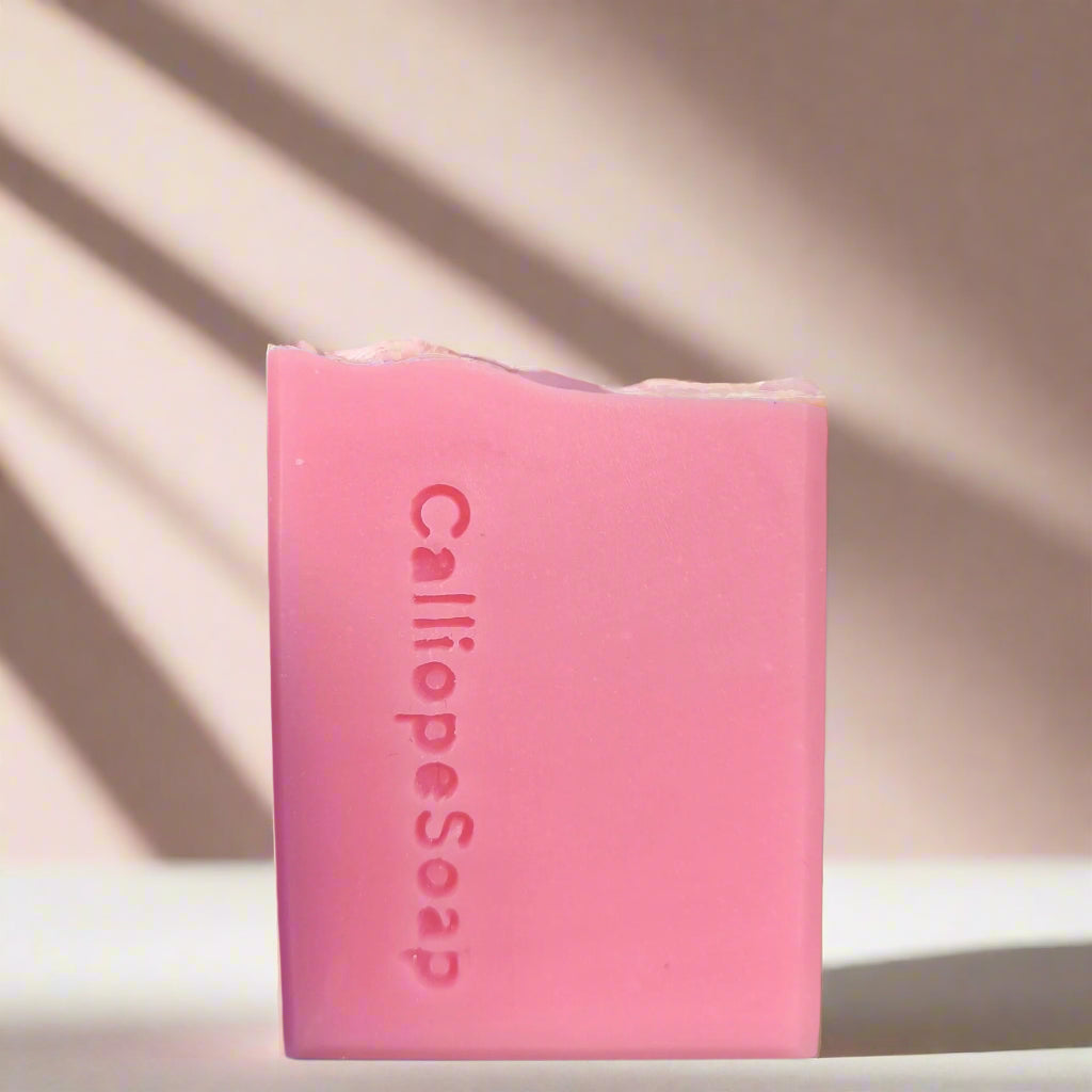 A bar of pink soap with a piece broken off, labeled 'CALLIOPE SOAP' on a shadowed background.