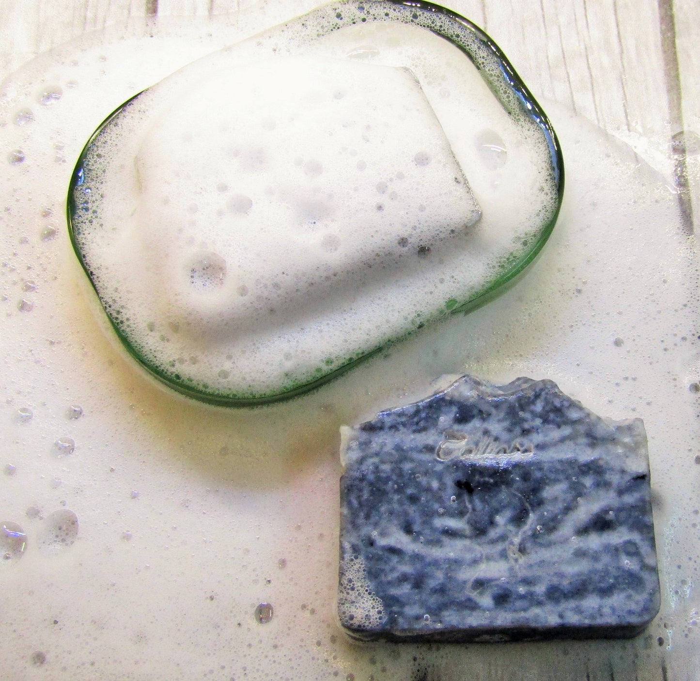 Two bars of men's soap, one with activated charcoal visible in the texture, displayed alongside a bubble of soap water.