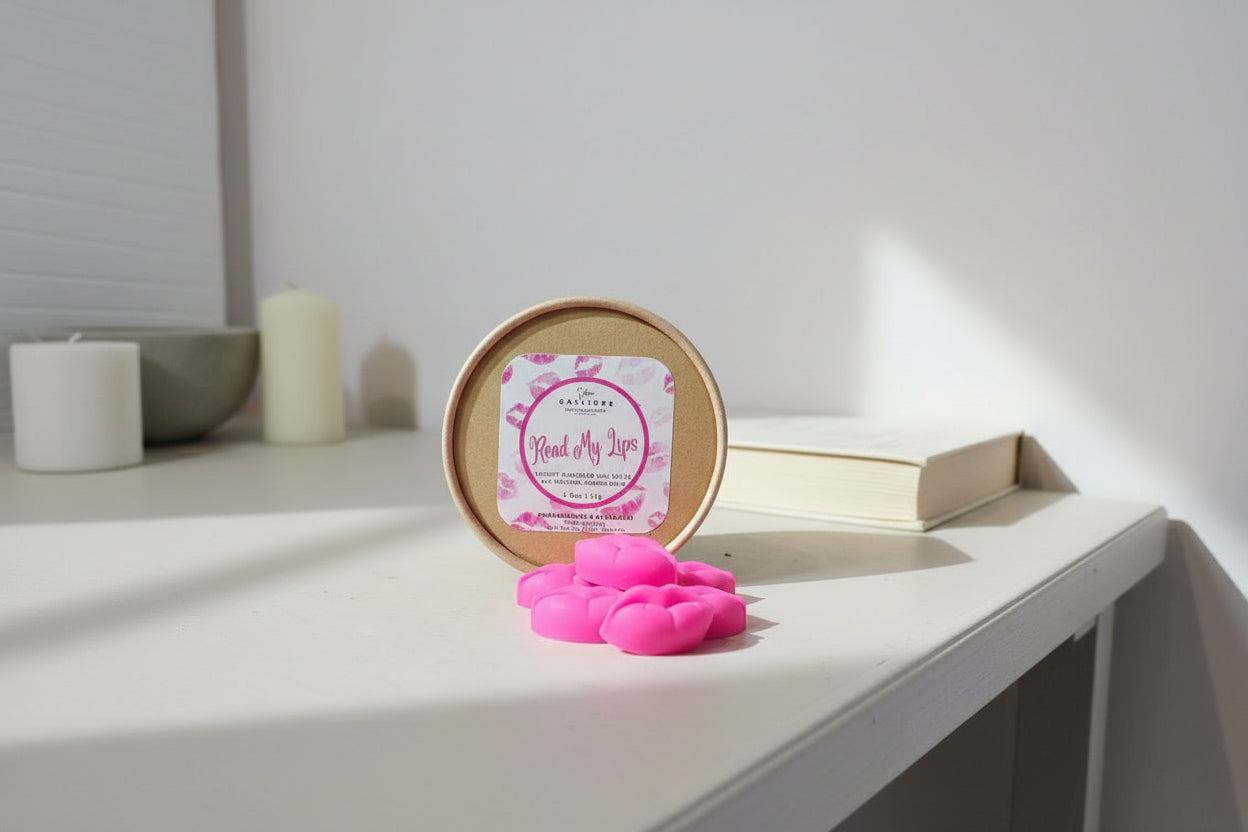 Pink lip-shaped wax melts in front of a round container with a label on a light surface.
