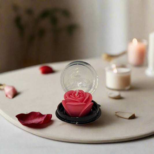 Three pillar candles with floral designs, in purple, pink, and red colors, set on a table with a window in the background.