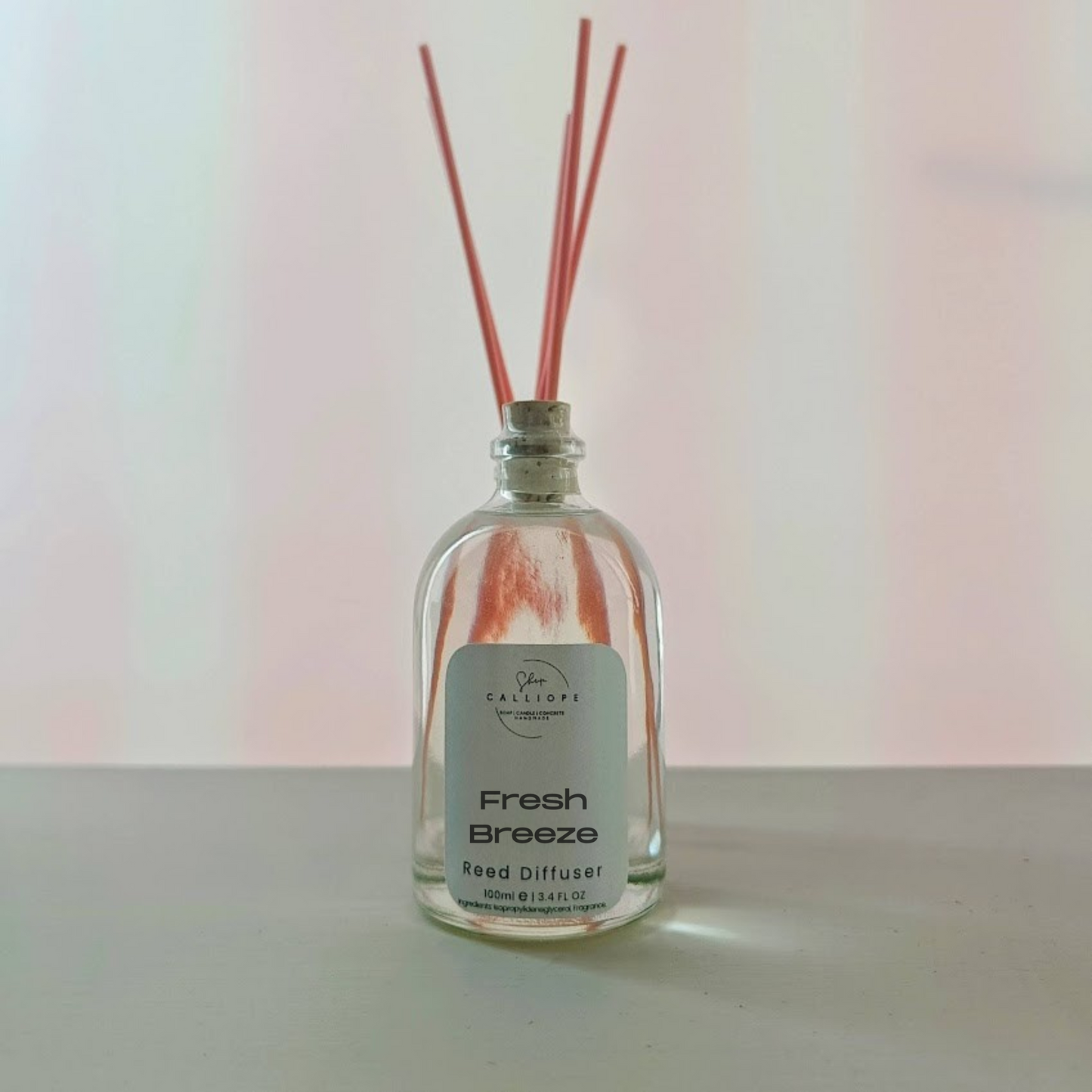 Clear glass diffuser bottle with pink reeds on a light background