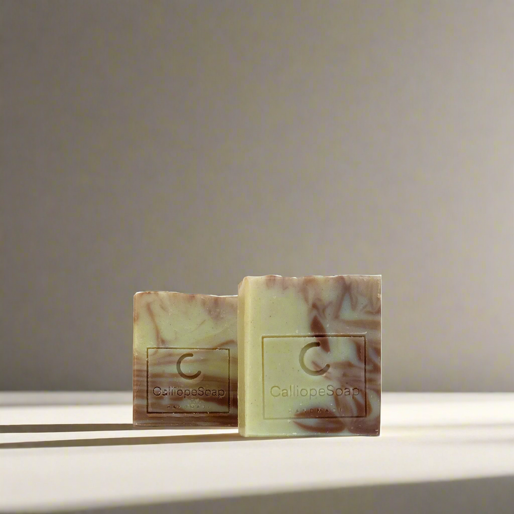 Two bars of handcrafted soap with a marbled pattern in shades of beige and white, each with a label indicating the brand 'Calliope Soap'.