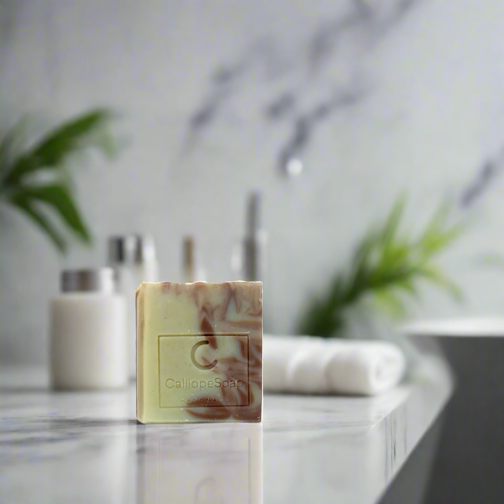 A bar of handcrafted soap with a marbled pattern in shades of beige and white, with a label indicating the brand 'Calliope Soap'.