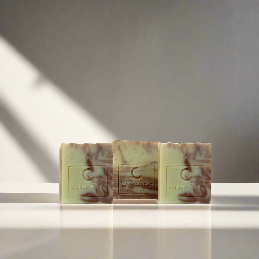 Three bars of handcrafted soap with a marbled pattern in shades of beige and white, each with a label indicating the brand 'Calliope Soap'.