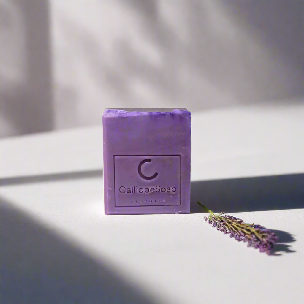 A bar of lavender-scented soap with 'CALLIOPE SOAP' branding, placed on a surface with some lavender flowers in the background.