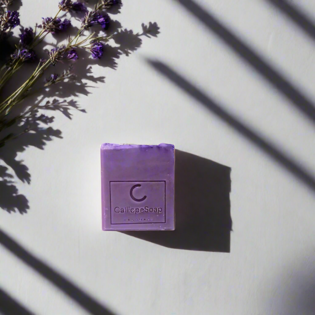 A bar of lavender-scented soap with 'CALLIOPE SOAP' branding, placed on a surface with some lavender flowers in the background.