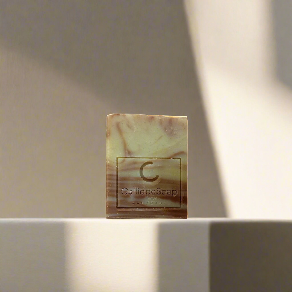 A bar of handcrafted soap with a marbled pattern in shades of beige and white, with a label indicating the brand 'Calliope Soap'.