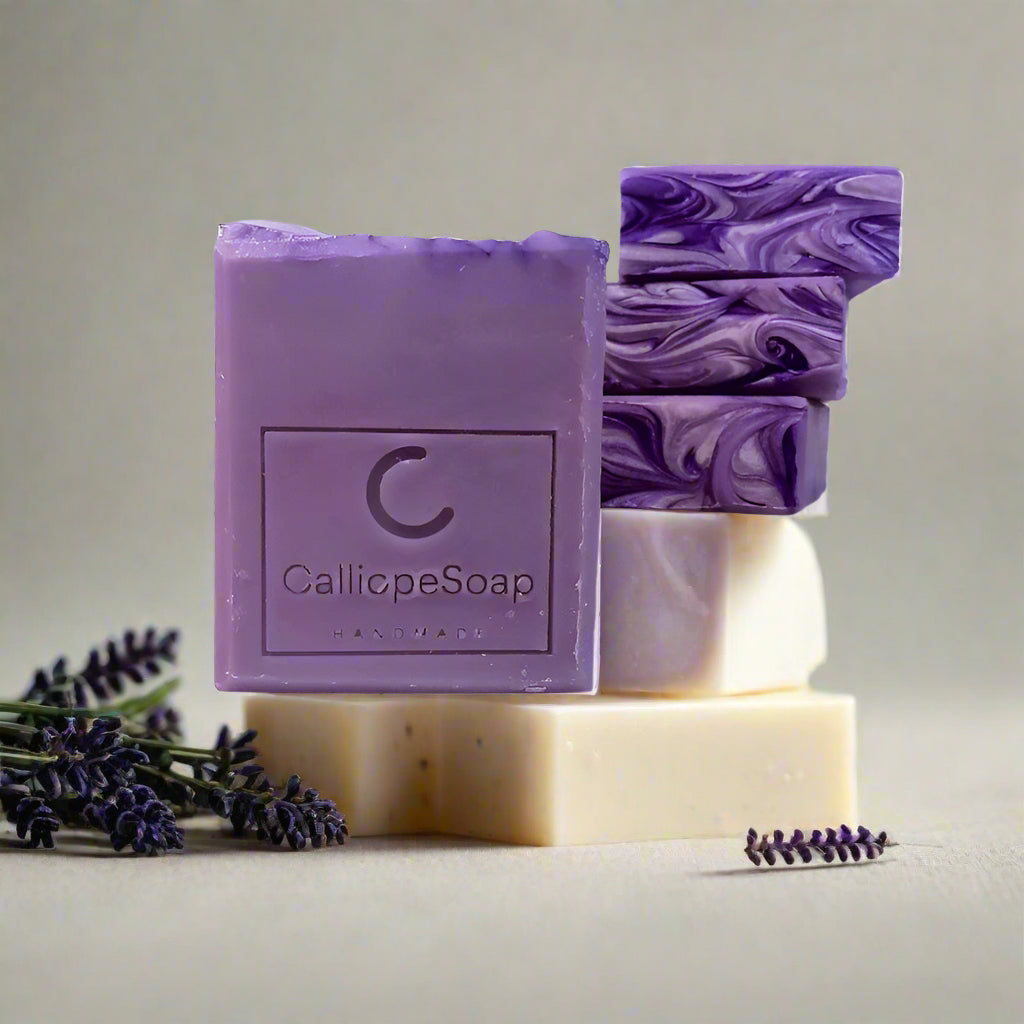 A bar of lavender-scented soap with 'CALLIOPE SOAP' branding, placed on a surface with some lavender flowers in the background.