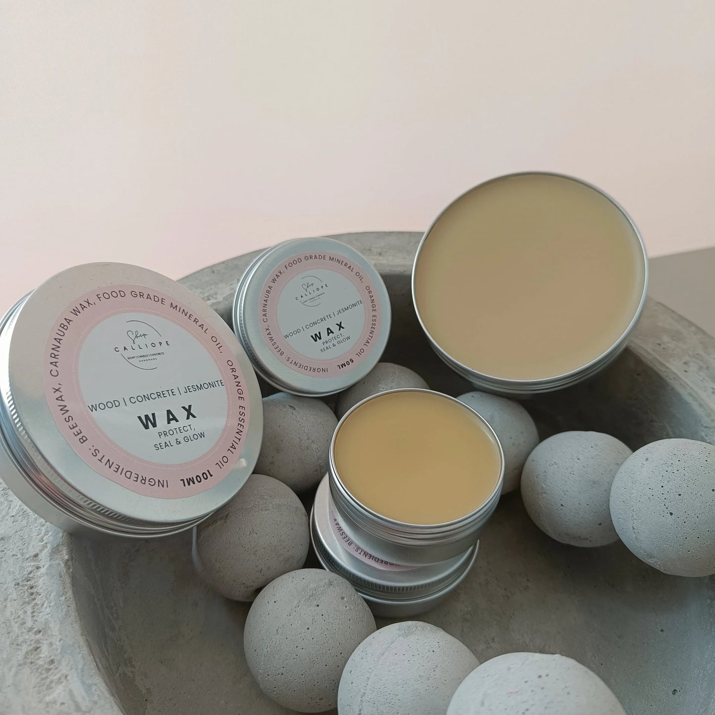 Tins of wax on a textured surface with a soft pink background