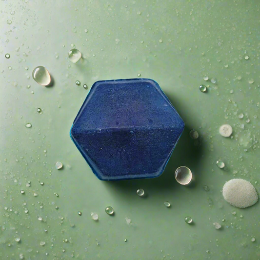 A blue hexagonal solid shampoo bar placed on a green surface with water droplets around it.
