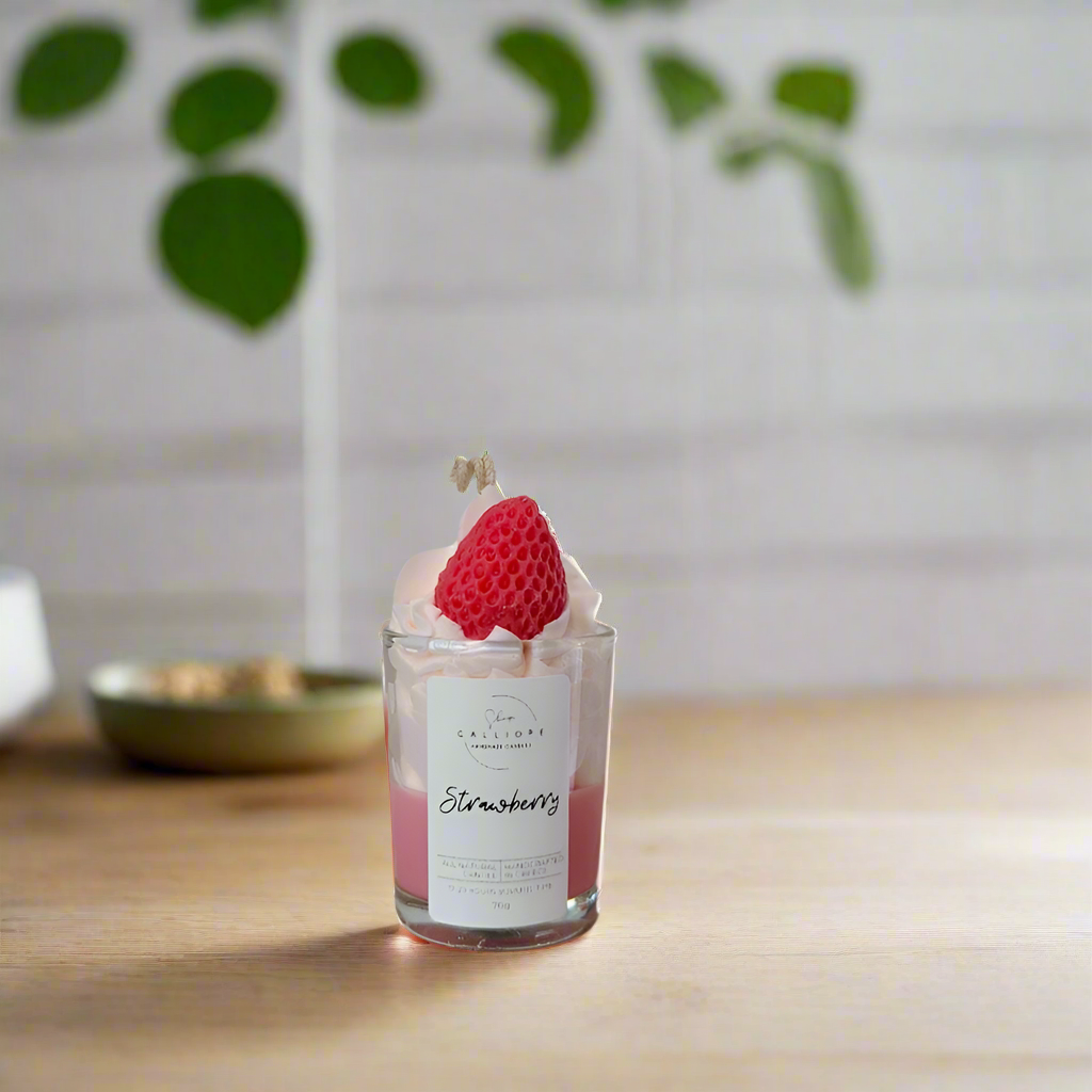 Candle shot with a strawberry decoration on a wooden surface with a blurred plant background