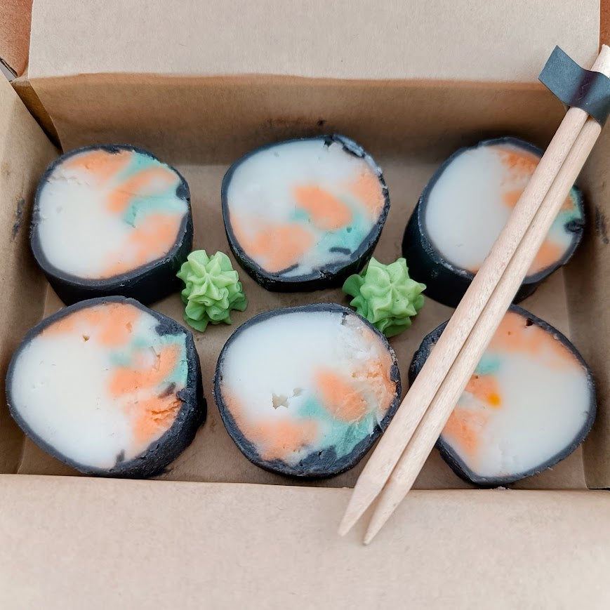 Sushi-like treats with colorful fillings in a cardboard box with chopsticks.