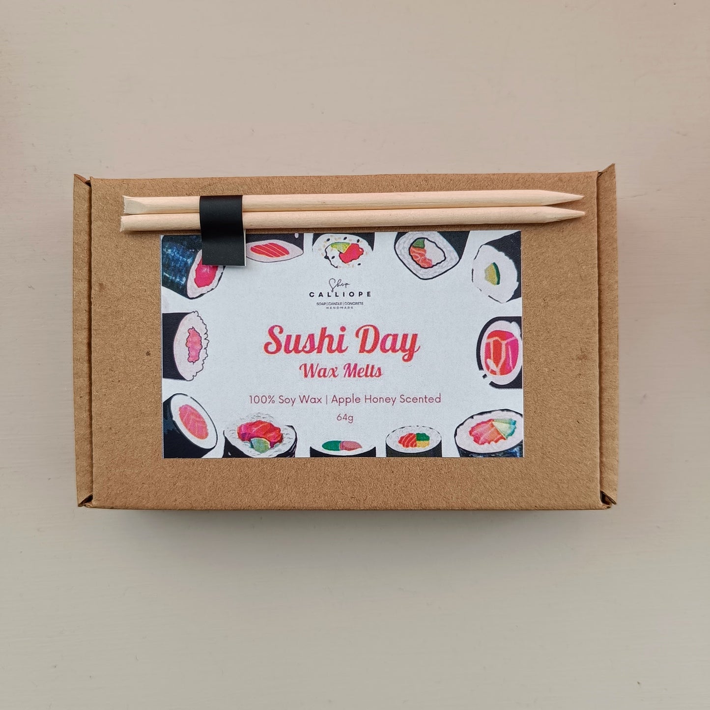 Box of 'Sushi Day' wax melts with wooden sticks on a beige background