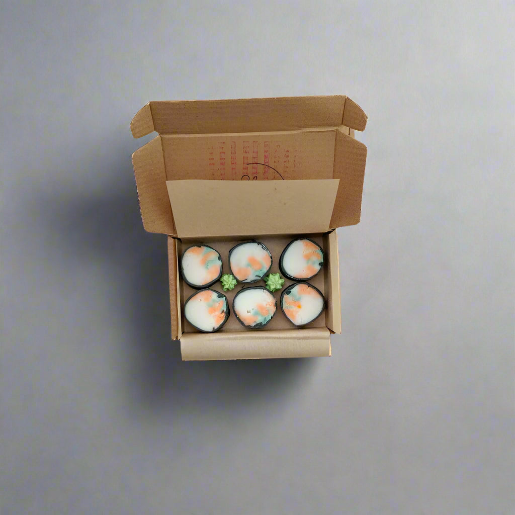 Open cardboard box containing six small round items on a light-colored surface.