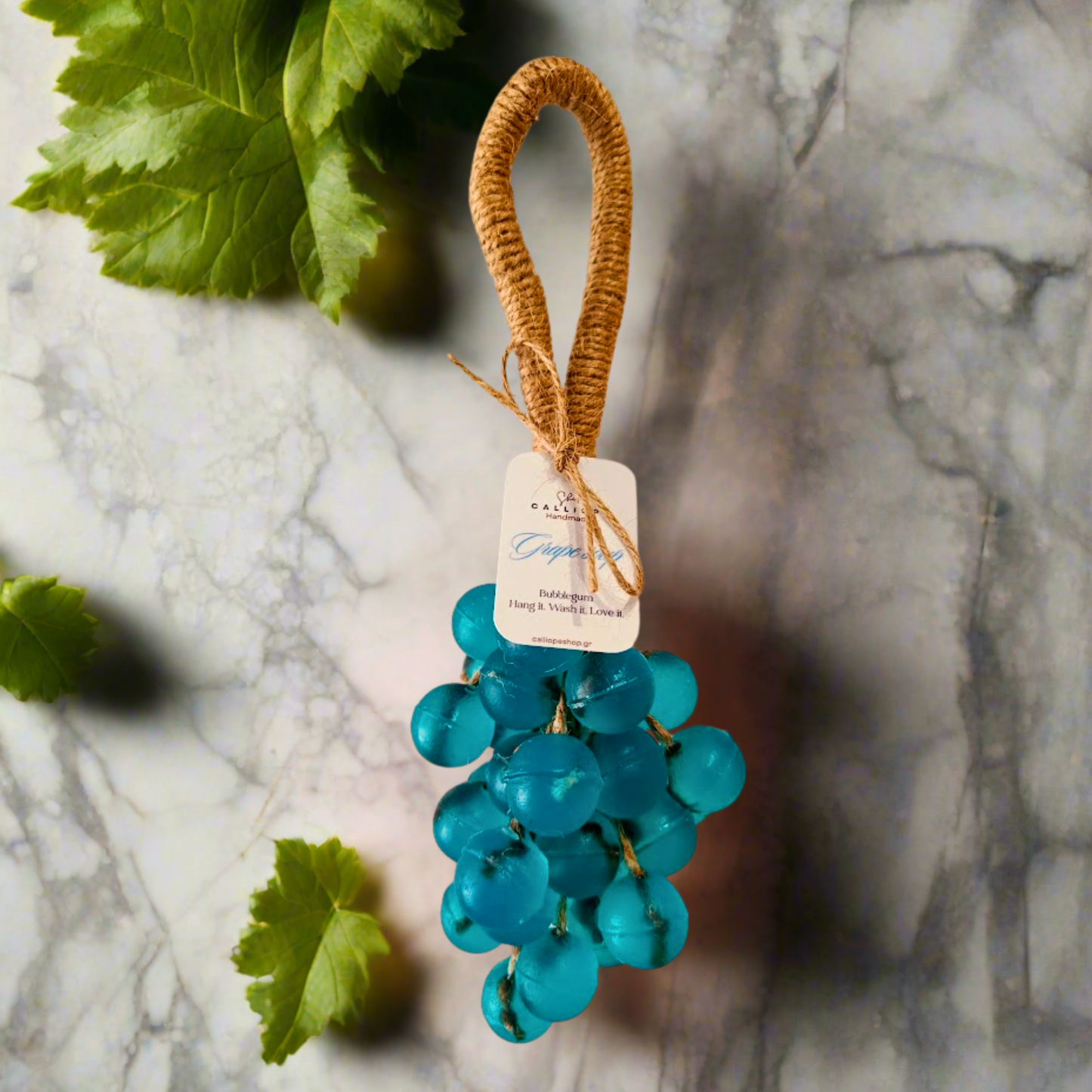 Decorative teal soap grapes with a brown handle on a marble surface