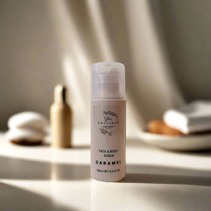 A white pump bottle labeled 'Face Scrub Caramel' with a capacity of 100ml, placed on a surface with a light caramel color, suggesting a natural or neutral tone. The product is marketed as a facial and body scrub.