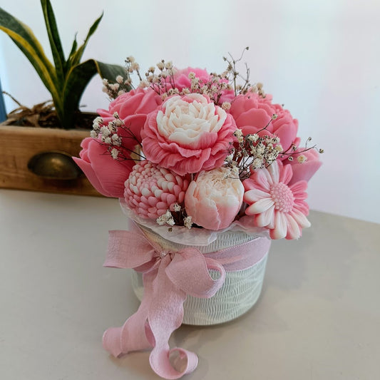 Pink and white floral arrangement in a small pot with a decorative bow on a light surface.
