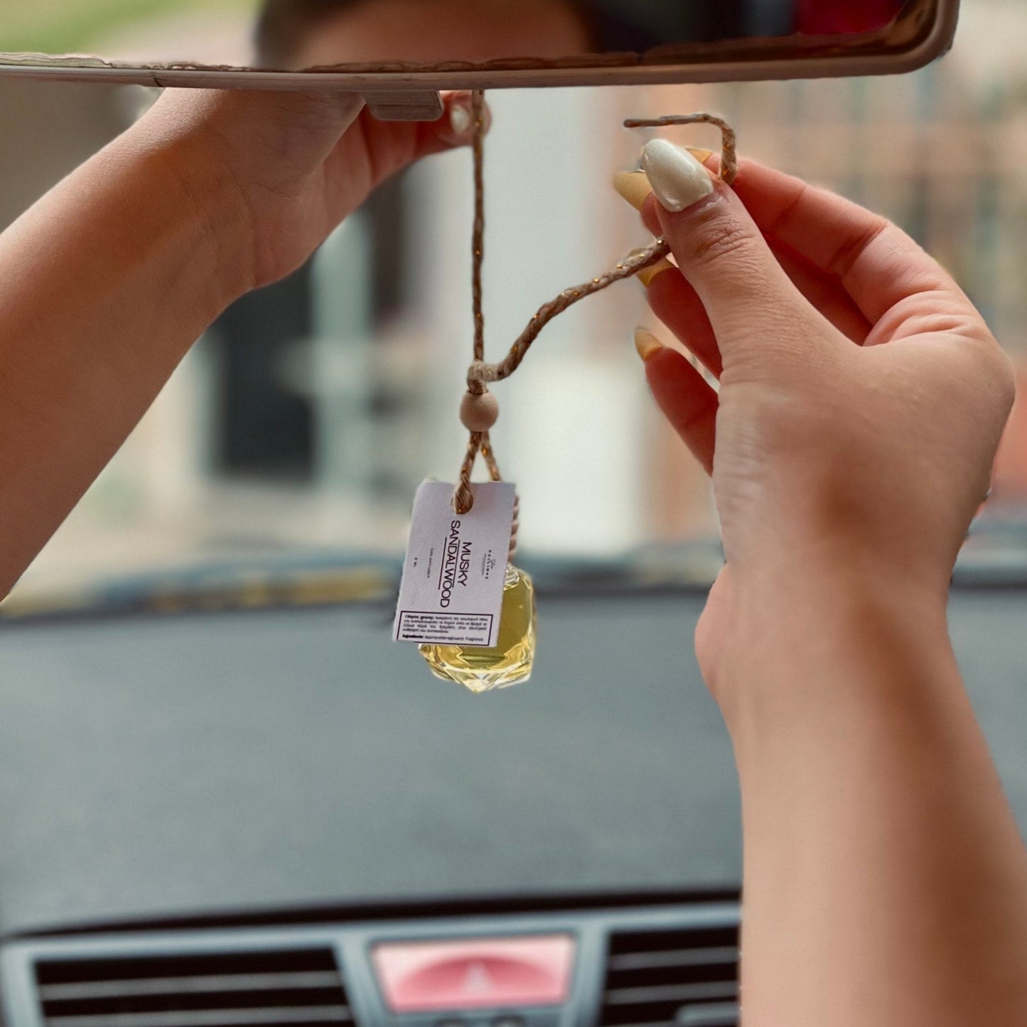 Person hanging a car air freshener from a car's rearview mirror.