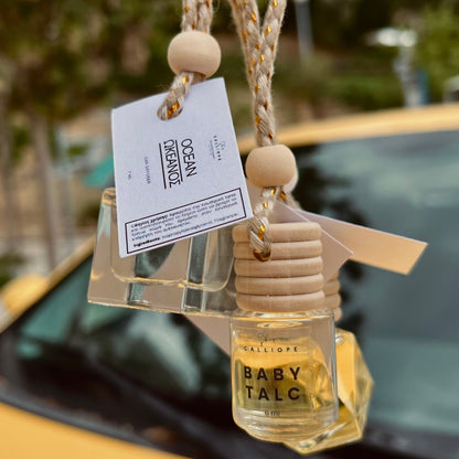 Car air freshener with 'Baby Talc' fragrance hanging from a rope on a car dashboard.
