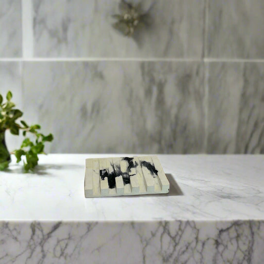 Handcrafted soap dish on a marble surface, minimalistic design, possibly with wooden material, accompanied by a bottle of liquid.